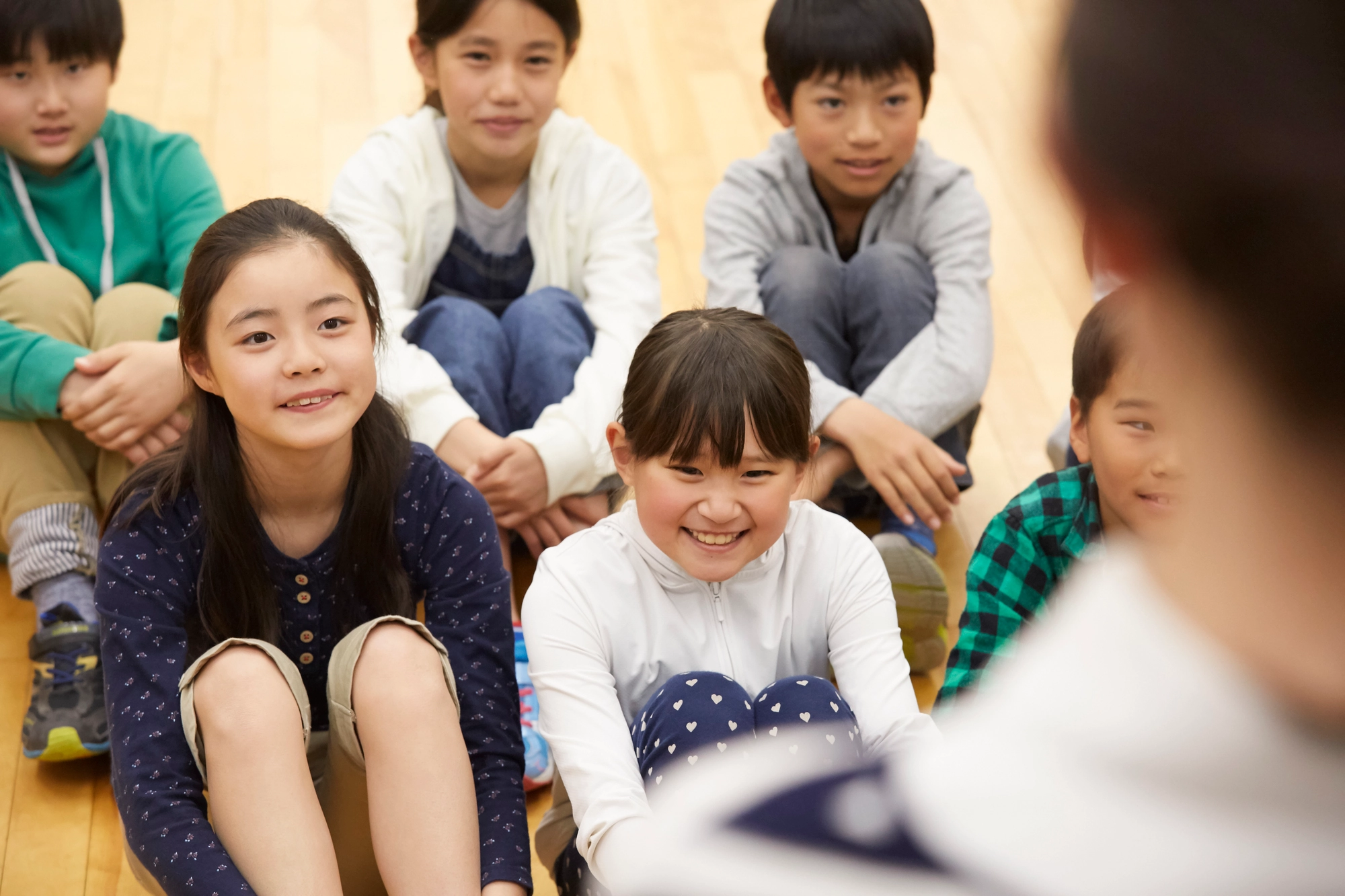 体育館で先生の話を聞く小学生の子どもたち