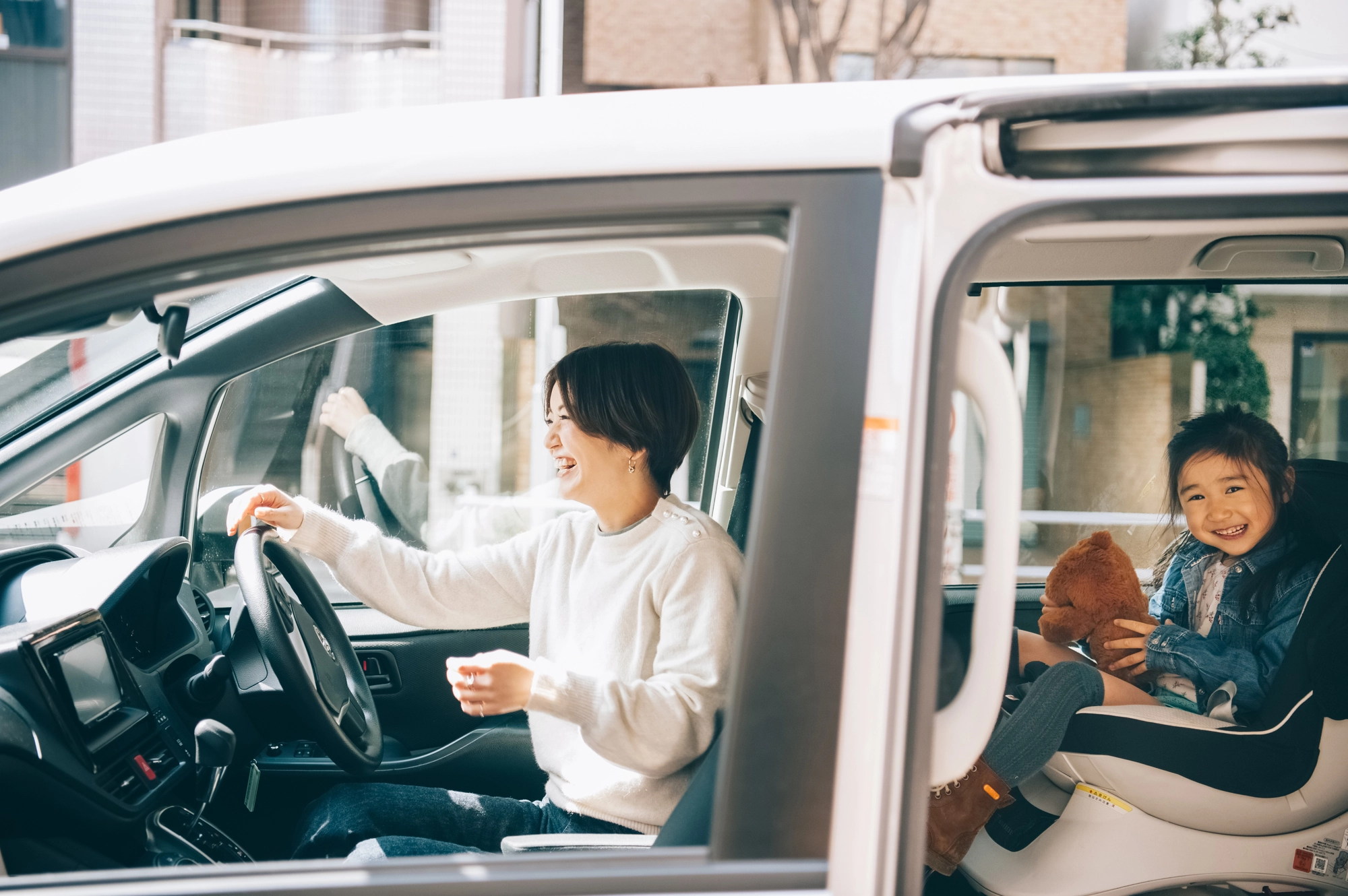 車の中でチャイルドシートに座り笑顔を見せる女の子と運転席の母親